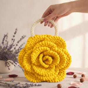 K&ouml;nnte beinhalten: Eine handgefertigte gelbe H&auml;keltasche in Rosenform. Die Tasche hat einen Griff aus wei&szlig;en Perlen. Die Tasche wird von einer Hand gehalten. Der Hintergrund umfasst Lavendel und Holzperlen.