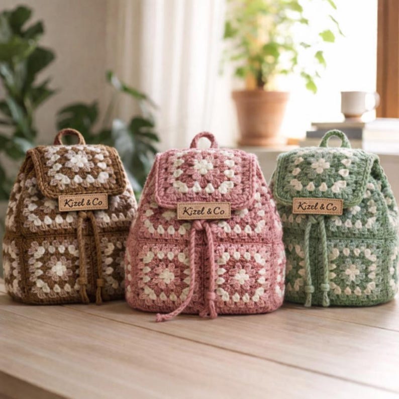 May include: Three crochet backpacks in brown, pink, and green, each with a square pattern and drawstring closure. The backpacks have a flap closure and a small leather tag that reads "Kizel & Co."
