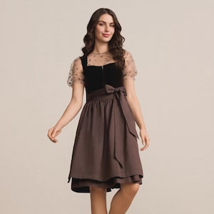 May include: A knee-length dirndl dress featuring a black velvet bodice with a front zipper, sheer short sleeves with a delicate pattern, and a solid brown skirt with a matching brown apron tied in a bow at the waist over a patterned underskirt.