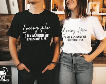 Könnte beinhalten: Ein Paar passende T-Shirts, eines in Schwarz und eines in Weiß. Das schwarze T-Shirt trägt den weißen Schriftzug "Loving Her is my assignment Ephesians 5:25". Das weiße T-Shirt trägt den schwarzen Schriftzug "Loving Him is my assignment Ephesians 5:25".