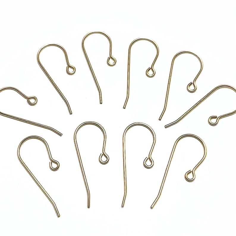 May include: Ten gold-toned earring hooks, also known as ear wires, are scattered on a white background. The hooks are made of metal and have a simple, classic design.