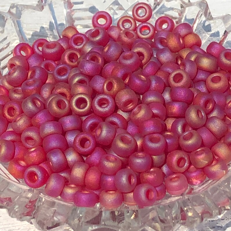May include: A bowl of small, round, iridescent pink and gold beads. The beads have a matte finish and are perfect for jewelry making.