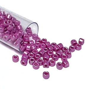 May include: A close-up of a small, clear plastic tube filled with pink, metallic seed beads. The beads are spilling out of the tube onto a white surface.