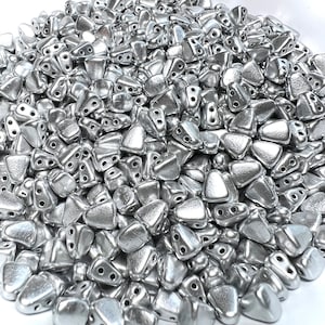 May include: A large pile of silver-colored triangle-shaped beads with two holes in each bead.