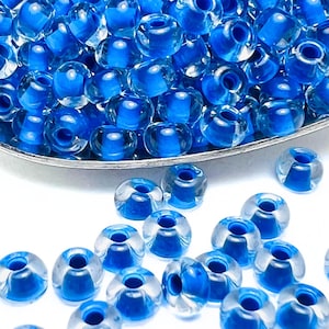 May include: A close-up of a pile of small, round, transparent glass beads with a blue center. The beads are scattered on a white surface.