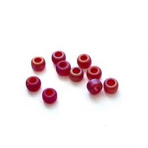 May include: A group of ten small, round, iridescent beads in shades of red and orange. The beads are scattered on a white surface.
