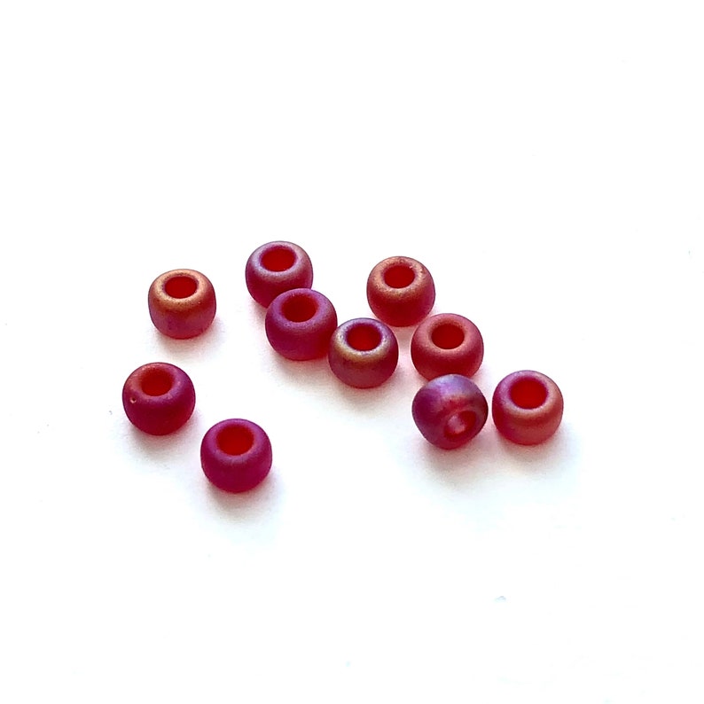 May include: A group of ten small, round, iridescent beads in shades of red and orange. The beads are scattered on a white surface.