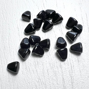 May include: A collection of black triangle-shaped beads. The beads are made of glass and have a glossy finish.
