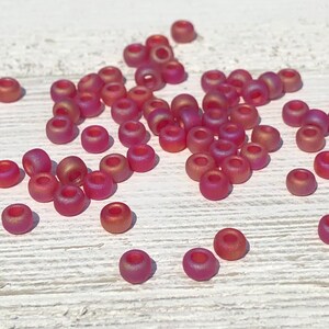 May include: A pile of small, round, iridescent pink beads. The beads are scattered on a white wooden surface.
