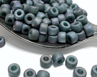 May include: A close-up of a pile of small, round, teal-colored glass beads. The beads have a matte finish and are arranged in a spoon.