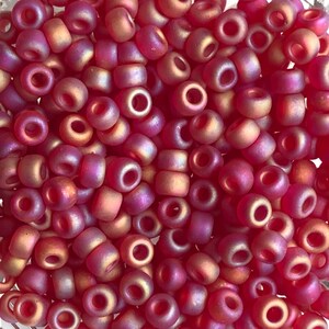 May include: A close-up of a pile of small, round, iridescent beads. The beads are a deep red color with a subtle shimmer. They are perfect for jewelry making or other craft projects.