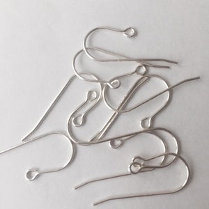 May include: A close-up of a pile of silver earring hooks. The hooks are made of metal and have a simple design.