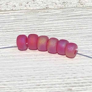 May include: A strand of eight small, round, pink glass beads with a slight iridescent shimmer. The beads are strung on a white thread.