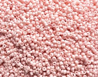 May include: A close-up image of a large quantity of small, round, pale pink beads. The beads are all the same size and shape, and they are arranged in a random pattern.
