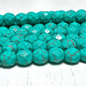 May include: Turquoise blue beads with a cracked, textured surface. The beads are round and have a slightly irregular shape.