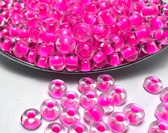 Puede incluir: Un montón grande de cuentas de semillas de vidrio rosa y transparente. Las cuentas son pequeñas y redondas, con un agujero en el centro. Las cuentas están dispuestas en un patrón aleatorio.