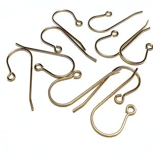 May include: A group of gold-colored earring hooks, also known as ear wires, are scattered on a white surface. The hooks are made of metal and have a simple, classic design.