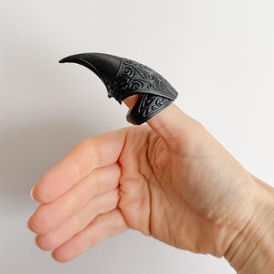 May include: Black claw-shaped finger armor with ornate scrollwork. The pointed tip extends from the finger, and the base features detailed patterns. The accessory is designed to be worn on a finger, adding a unique and edgy aesthetic.