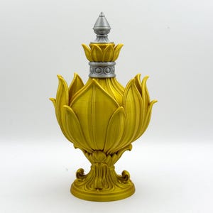 Könnte beinhalten: Eine weiße Keramik-Tasse mit schwarzem Henkel und dem Text "But First, Coffee" in fetter, schwarzer Schrift. Die Tasse steht vor einem verschwommenen Hintergrund, der eine gemütliche Umgebung suggeriert.