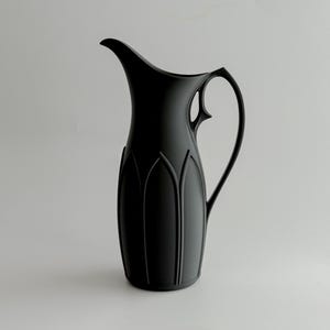 May include: A matte black pitcher with a slender handle and a curved spout. The body of the pitcher features vertical, arched grooves. The design is minimalist and elegant, suitable for serving beverages.