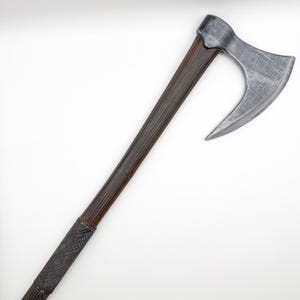 May include: A detailed axe featuring a dark wooden handle and a silver-coloured blade. The handle has a textured grip near the base. The axe head is curved. The design suggests a historical or fantasy theme, with a focus on craftsmanship.