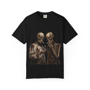 May include: Black t-shirt featuring a graphic of two skeletons smoking cigarettes. One skeleton is holding a lighter. The skeletons are depicted in a realistic, detailed style. The t-shirt is made of a soft, comfortable material.