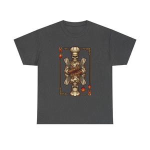 May include: Dark gray t-shirt featuring a playing card design. The card depicts a skeleton chef holding crossed cleavers, with a chef's hat and the letter "K". The card is framed in a gold border with the suit of hearts.