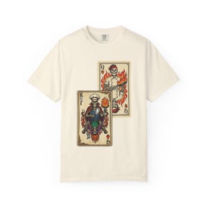 May include: Cream-colored t-shirt featuring two playing cards with skeleton chefs. The King card shows a skeleton in a chef's hat and cape, while the Queen card depicts a skeleton holding a gun, both surrounded by flames. The cards are in a vintage tattoo style.