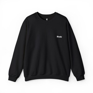 Puede incluir: Sudadera negra de cuello redondo y manga larga. La palabra "Woabit" está impresa en blanco en la parte delantera. Un pequeño gráfico blanco es visible cerca del escote. La sudadera es de color negro liso.