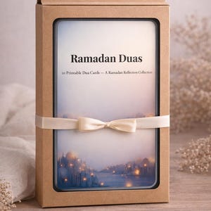 Puede incluir: Una caja rectangular de cartón marrón claro, atada con una cinta crema y un lazo. Contiene una tarjeta enmarcada con las palabras "Ramadan Duas" y una imagen de acuarela de una ciudad al atardecer. La caja está cerrada.