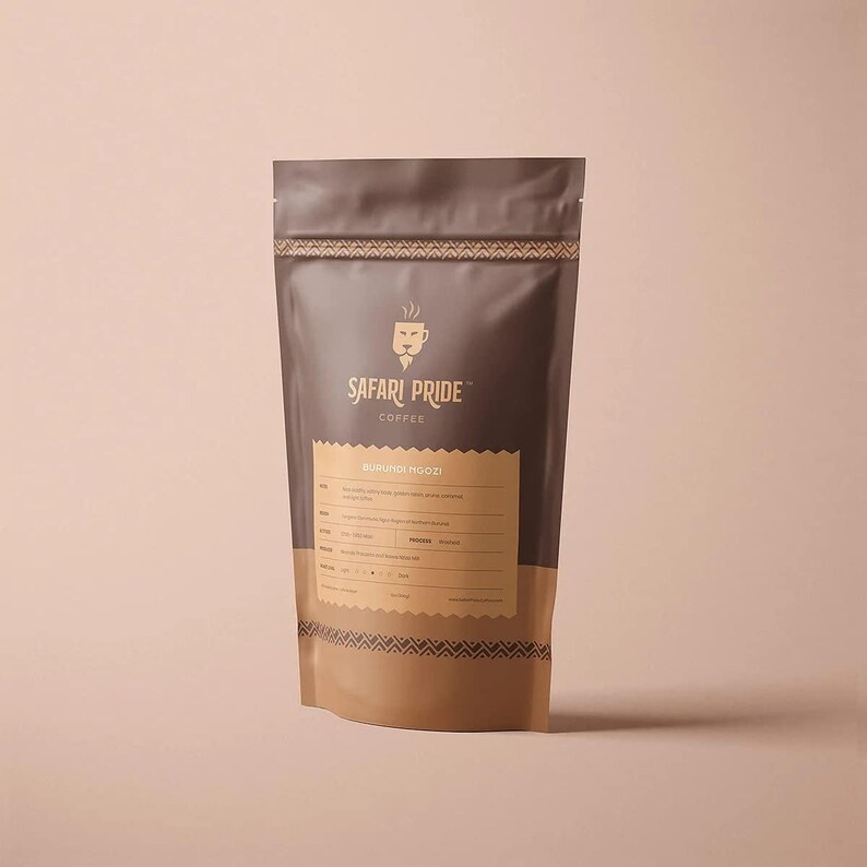 May include: A brown and tan coffee bag with the text "Safari Pride Coffee" and a lion logo. The bag also has the text "Burundi Ngozi" and other details. The bag is standing upright against a light pink background.