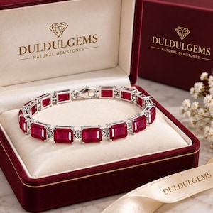 May include: A silver-toned link bracelet featuring rectangular, deep red gemstones set in a row. The bracelet is displayed inside an open, dark red velvet-lined box with the text DULDULGEMS NATURAL GEMSTONES printed on the interior lid and exterior.