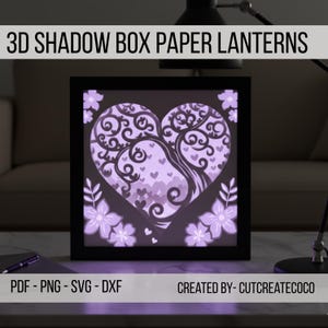 May include: A 3D shadow box paper lantern with a heart-shaped design featuring a tree and floral accents. The lantern is illuminated with a soft purple glow, and the frame is black. Text on the image reads "3D SHADOW BOX PAPER LANTERNS" and "PDF - PNG - SVG - DXF".