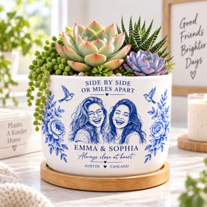 May include: A white ceramic planter on a bamboo saucer containing various succulents. The planter features blue floral illustrations, two birds, and text reading: SIDE BY SIDE OR MILES APART, EMMA & SOPHIA, Always close at heart, AUSTIN & CHICAGO.