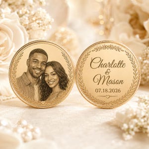May include: Two circular gold-toned metal coins featuring engraved designs. One coin displays a portrait of a couple, while the other features the text Charlotte & Mason, the date 07.18.2026, and a decorative laurel wreath border with small hearts.