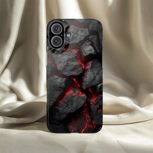 Può includere: Custodia per telefono nera con un design strutturato di rocce grigio scuro con fessure rosse brillanti. La custodia ha una finitura lucida e un ritaglio per un sistema a doppia lente.