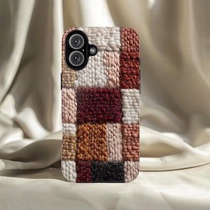 Puede incluir: Una funda de teléfono con un diseño de patchwork. La funda presenta un patrón texturizado de cuadrados en varios colores, incluyendo blanco, beige, marrón y burdeos. La funda del teléfono tiene un módulo de cámara con dos lentes.