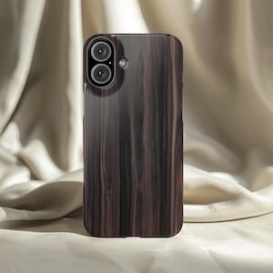 Könnte beinhalten: Dunkelbraune Handyhülle mit Holzmaserung. Die Hülle hat einen Ausschnitt für eine Dual-Objektiv-Kamera und eine glänzende Oberfläche. Der Hintergrund ist ein weicher, neutraler Stoff.
