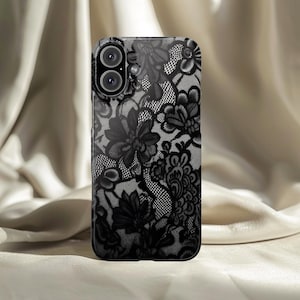 Puede incluir: Funda de teléfono negra con un diseño de encaje floral. La funda tiene un acabado brillante y un recorte para la cámara. El patrón de encaje incluye varias formas de flores y hojas.