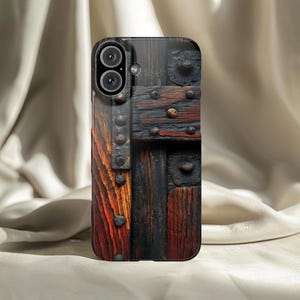 May include: A phone case featuring a detailed wood grain design with dark brown and reddish-brown tones. The case has a textured appearance with metal accents, giving it a rustic, vintage aesthetic. The case has a dual-lens camera cutout.