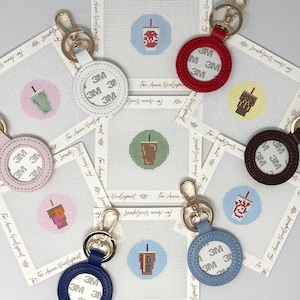 Puede incluir: Llaveros con detalles de cuero en varios colores, cada uno con un cierre dorado. Los llaveros tienen un diseño circular con una pegatina 3M y se combinan con lienzos de punto de aguja que representan diseños de bebidas.