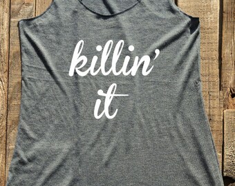 May include: A gray racerback tank top with the phrase "killin' it" printed in white. The tank top is made of a soft material and has a scoop neck. The text is in a cursive font.