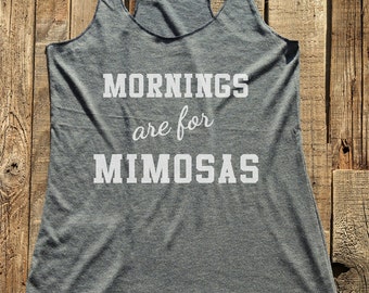 May include: A gray racerback tank top with the text "Mornings are for Mimosas" in white block letters. The tank top is made of a soft material and has a scoop neck. The background is a rustic wooden surface.