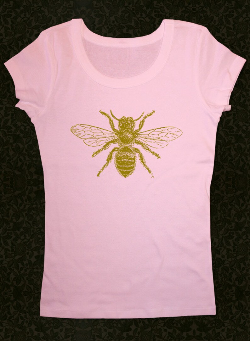 Op de afbeelding: Een roze T-shirt met een gouden bij-print op de voorkant.