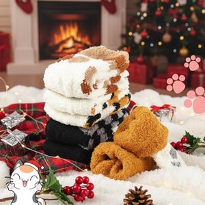 May include: A stack of cozy, patterned socks in various colors, including white, brown, black, and gold. The socks are displayed on a fluffy white surface with a plaid blanket, Christmas tree, and a fireplace in the background. The text "Holiday Comfort!" is visible.