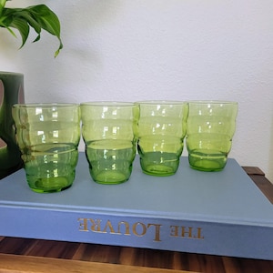 May include: A set of four translucent lime green drinking glasses with a distinct horizontal ribbed texture. Each glass features a tapered shape with rounded ridges along the sides, providing a consistent look across the collection of glassware.