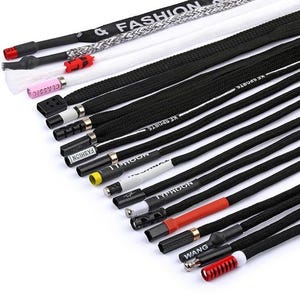 Puede incluir: Surtido de cordones negros y blancos con varios diseños en los extremos. Algunos cordones tienen texto que dice "& FASHION", "CLASSIC", "KE SPORTS", "TYPHOON" y "WANG". Los cordones están hechos de material tejido.