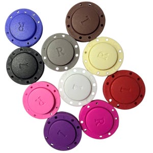 May include: A collection of ten circular magnetic snap buttons in various colors including blue, brown, gray, cream, black, white, red, pink, purple, and magenta. Each button features a raised letter R or L embossed on the center surface.