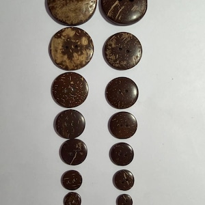 May include: A collection of coconut shell buttons in various sizes. The buttons range in color from light brown to dark brown, with visible natural grain patterns. Each button has two or four holes for sewing.