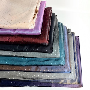 Puede incluir: Una pila de cuadrados de tela doblados en varios colores, incluyendo crema, lavanda, burdeos, negro, gris, verde azulado y azul. Cada pieza de tela presenta un patrón consistente de pequeños puntos espaciados uniformemente por la superficie.